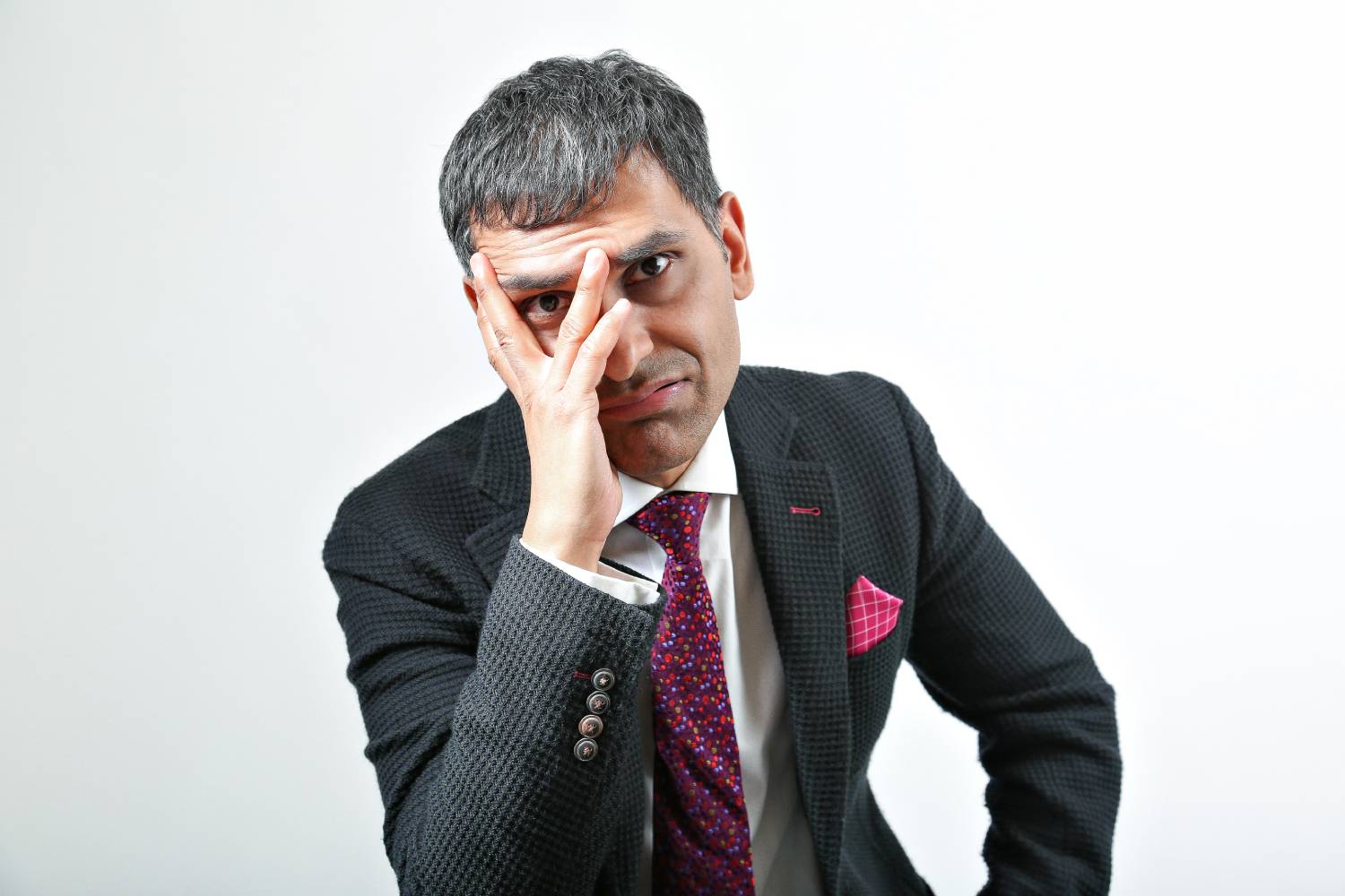 An image of Harry, wearing a black suit jacket, a red and pink spotty tie and a pink pocket square. He is looking at the camera with a concerned expression.